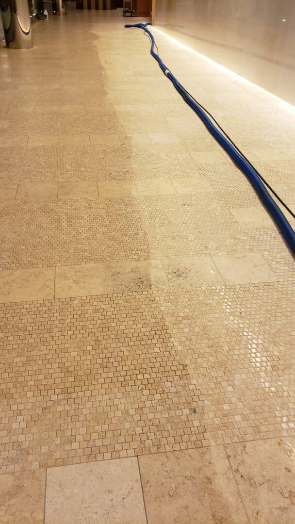 A tiled floor in the gallery being cleaned with a blue hose.